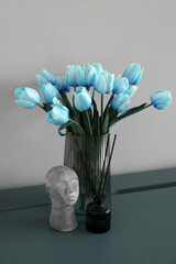 Vase with beautiful tulips, stylish decor and reed diffuser on table near grey wall