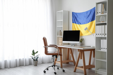 Interior of modern office with workplace, shelving units and hanging Ukrainian flag