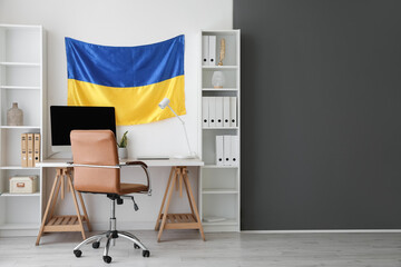 Interior of modern office with workplace, shelving units and hanging Ukrainian flag