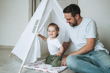 Happy father young man and baby girl little daughter having fun playing in wigwam in children room at home © Galina Zhigalova