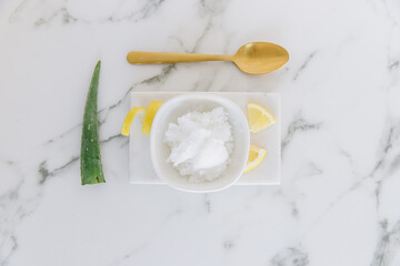 Coconut oil in a bowl with aloe Vera and lemon slices. Objects are on a rectangular object with marble table.