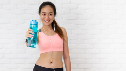 Asian beautiful women holding water bottle after play yoga and exercise on white brick wall...