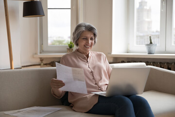 Happy homeowner woman doing domestic paperwork, accounting work, using laptop computer, making online payment, paying insurance, mortgage fees, checking expenses