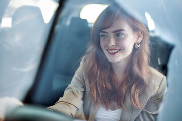 Beautiful young woman driving her new car at sunset. Woman in car. Close up portrait of pleasant looking female with glad positive expression, woman in casual wear driving a car