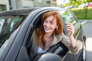 Beautiful young woman driving her new car at sunset. Woman in car. Close up portrait of pleasant looking female with glad positive expression, woman in casual wear driving a car - obrazy, fototapety, plakaty