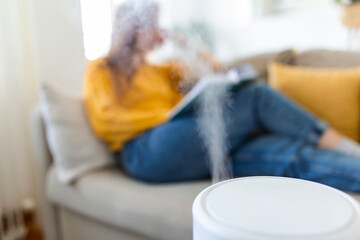 Air purifier in cozy white Living room for filter and cleaning removing dust PM2.5 HEPA at home with woman reading a book on sofa,for fresh air and healthy life,Air Pollution Concept - obrazy, fototapety, plakaty