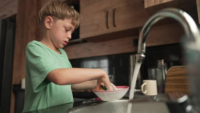Little boy washing dishes in kitchen. Baby Dish Washing.