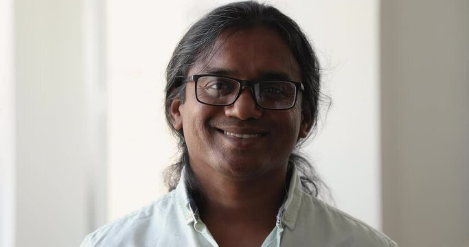 Headshot face portrait intelligent smiling long haired Indian male in eyeglasses worker teacher business owner corporate expert. Confident handsome businessman engineer pose in office look at camera