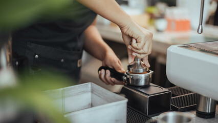 Barista using a tamper to press ground coffee into a portafilter. Close-up view on barista hands to making coffee with coffee machine. Coffee owner concept.