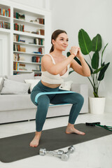 Fototapeta na wymiar Active young woman doing morning exercises squatting alone in the living room, serious girl in sportswear doing squat muscle training at home for body healthy lifestyle concept