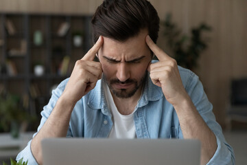 Mental tension. Stressed male sit by pc contemplate think hard with closed eyes touch forehead with...