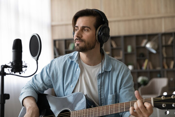 Performing song. Inspired man singer and music writer amateur sit in earphones hold guitar work on...