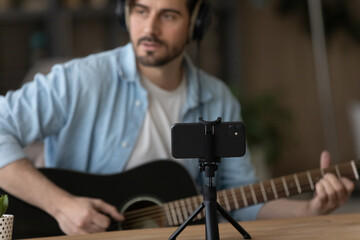 Young man musician play song on guitar take part in online music contest at social media using video app on phone. Millennial guy blogger influencer create audio content for channel using cell webcam