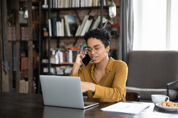 African woman sit at desk looks at laptop booking hotel, plan vacation talking to on-line...