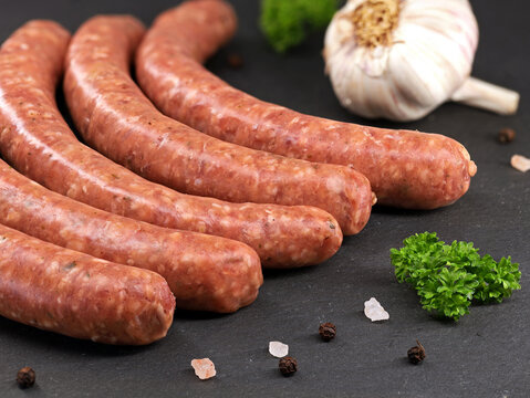 Raw veal sausages with parsley, garlic and spices on black slate, close up of delicious red sausages ready for grilling