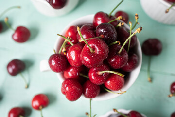 Delicious cherries in white ceramic cups on a light green wooden table