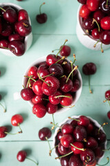 Delicious cherries in white ceramic cups on a light green wooden table