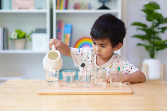 A 3 years old asian little boy pouring the water to the cup in montessori class, concept of homeschool, practical life skill, kid learning activity, freedom, education for kid development.