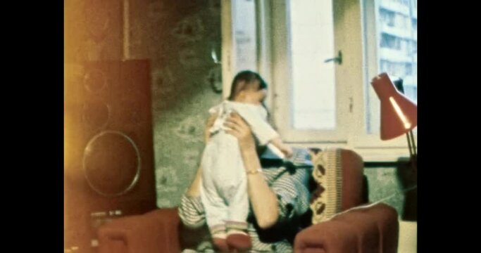 Happy young mother playing with her child at home apartment. Smiling baby with mom. Woman's love for child. Vintage color film. Cinema lens flare. Retro 80s, 90s overscan of family archive 8mm. 4k 