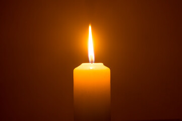 A single burning candle flame or light glowing on a yellow candle isolated on red or dark...