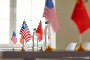 Obraz na płótnie Canvas Flags of China and America on conference table symbolizing cooperation between two countries. Flagpoles with flags of countries participating in meeting and bottles of water on table in meeting room.