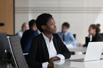 African businesswoman looks into distance thinks or daydreams distracted from work sit at desk with laptop, feels satisfied by promotion and career growth. Business aspirations, vision, plans concept