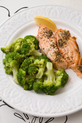Grilled salmon served with broccoli and a piece of lemon on white plate. Vegetarian lunch for diet.