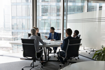 Fototapeta na wymiar Serious team of professionals, five multi ethnic business people negotiating in modern boardroom, discuss project, consider contract terms and conditions, solve business. Formal meeting event concept