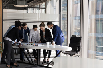 Group of multi ethnic teammates gathered together for project financial stats discussion, do paperwork at meeting briefing, diverse employees brainstorm cooperate in office boardroom, teamwork concept