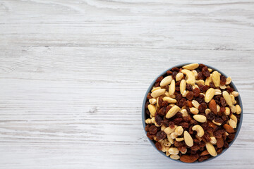 Raw Trail Mix with Nuts and Fruits in a Bowl on a white wooden background, top view. Flat lay, overhead, from above. Copy space.