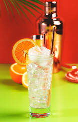 Tom Collins popular alcoholic cocktail with dry gin, syrup, lemon juice, soda, orange and ice. Bright red green summer background, negative space