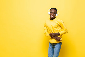 Positive happy African man listening to music on headphones in yellow color studio isolated background with copy space