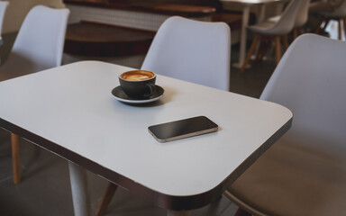 A single mobile phone and coffee cup on the table in cafe