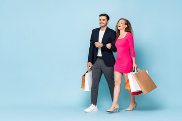 Happy Caucasian couple with shopping bags walking in studio light blue color isolated background...