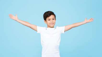 Cute smiling handsome mixed race boy with open arms in isolated light blue color studio background - obrazy, fototapety, plakaty