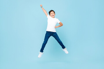 Fototapeta na wymiar Cheerful Asian mixed race boy jumping and raising hand up in isolated light blue color studio background
