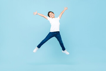 Fototapeta na wymiar Energetic Asian mixed race boy jumping and raising hands up in isolated light blue color studio background