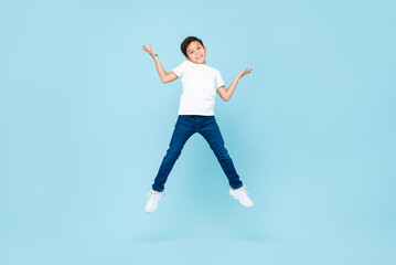 Fototapeta na wymiar Cute Asian mixed race boy jumping and shrugging shoulders in isolated light blue color studio background