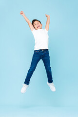 Cheerful Asian mixed race boy jumping and raising hands up in isolated light blue color studio...