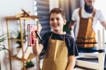 Cheerful young male carpenter and his son working in workshop