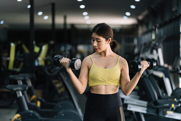 Fototapeta na wymiar Beautiful young Asian woman doing exercises in gym to stay fit. Fit female exercising with dumbbell weights.