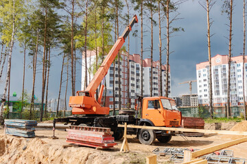 A truck crane at a construction site is ready to lift loads. Construction of a new residential area on the outskirts of the city in a forested area.