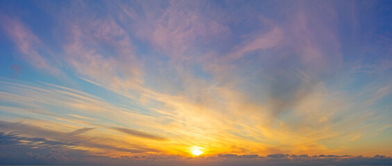 Panoramic view of the sky with different types of clouds gradient illuminated by the evening sun leaving the horizon.