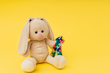 Toy bunny with puzzle pattern ribbon on a yellow background. World autism awareness and pride day.