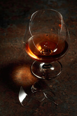 The drop of brandy falls into a broken glass.
