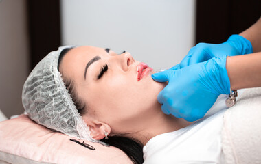 Obraz na płótnie Canvas Lip augmentation. Beautician injects hyaluronic acid into the lips of a girl with a syringe. The cosmetologist doctor performs the procedure in the cosmetology office. Plastic surgery.