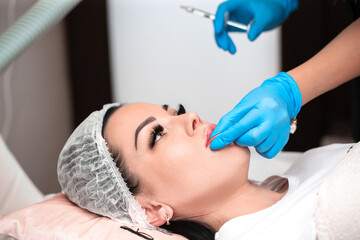 Fototapeta na wymiar Lip augmentation. Beautician injects hyaluronic acid into the lips of a girl with a syringe. The cosmetologist doctor performs the procedure in the cosmetology office. Plastic surgery.