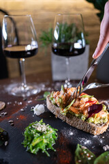 person eats fresh sandwich with avocado, red salmon fried fish, seaweed, wine