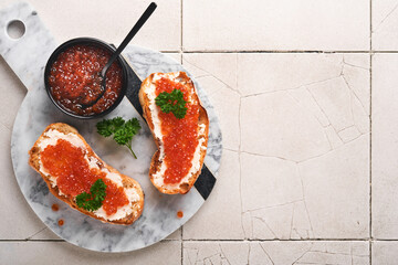 Red caviar sandwiches. Salmon red caviar in bowl and sandwiches on marble plate on old gray cracked tile table background. Top view. Copy space.