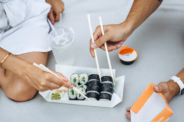 Young couple eating sushi sitting outdoors.